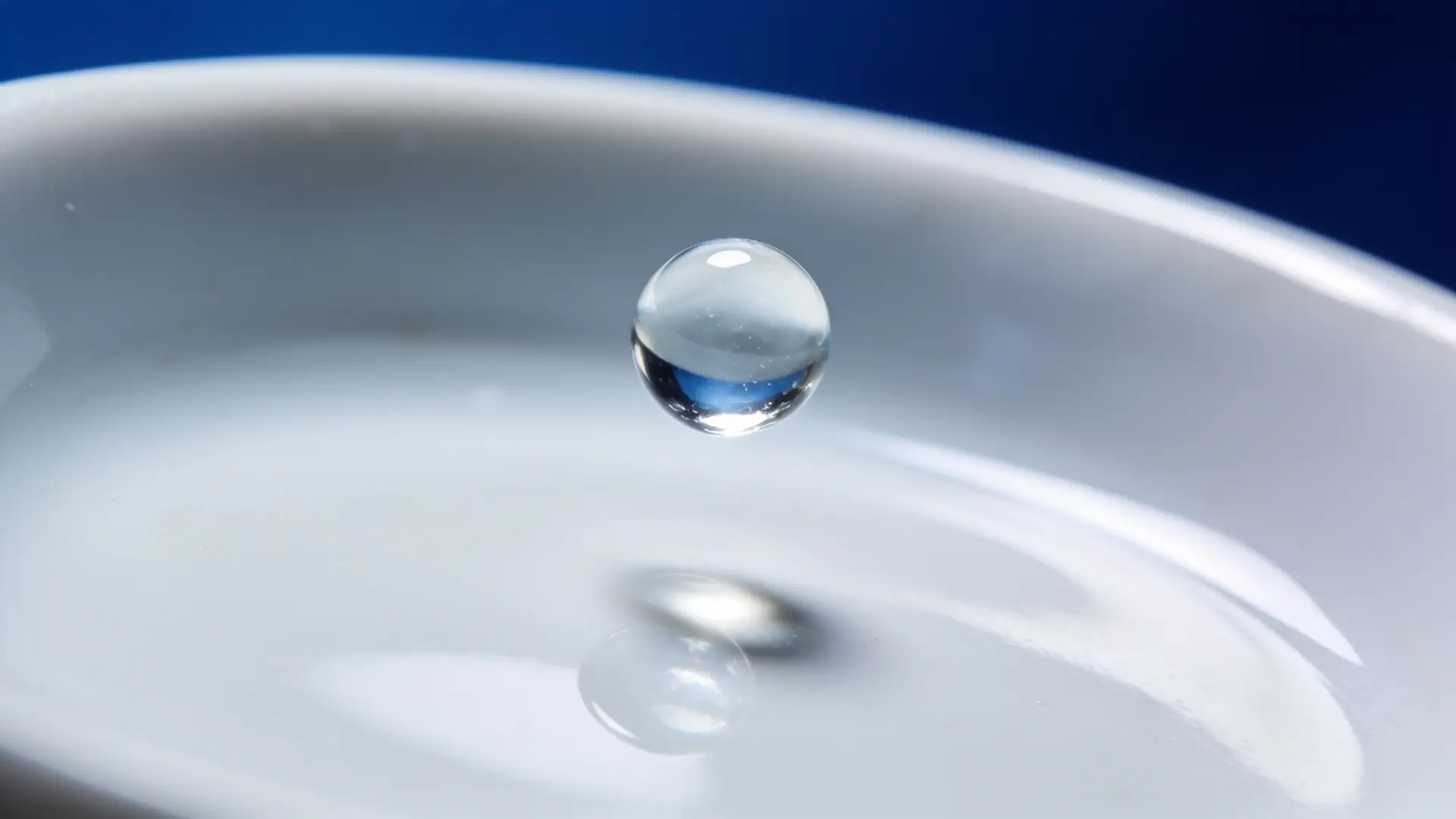 A single clear gel droplet above porcelain, lit in blue