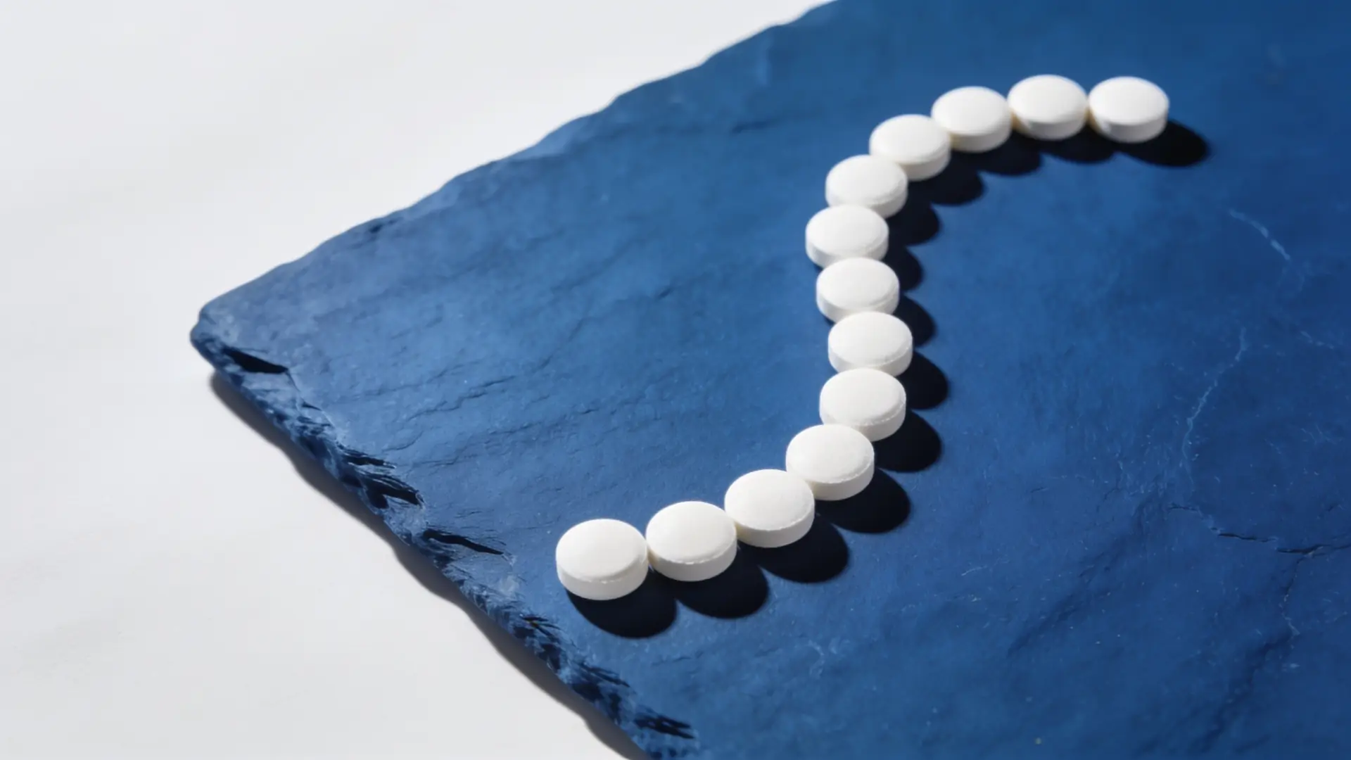 Small white tablets in an arc on blue slate — illustrative image for finasteride and dutasteride