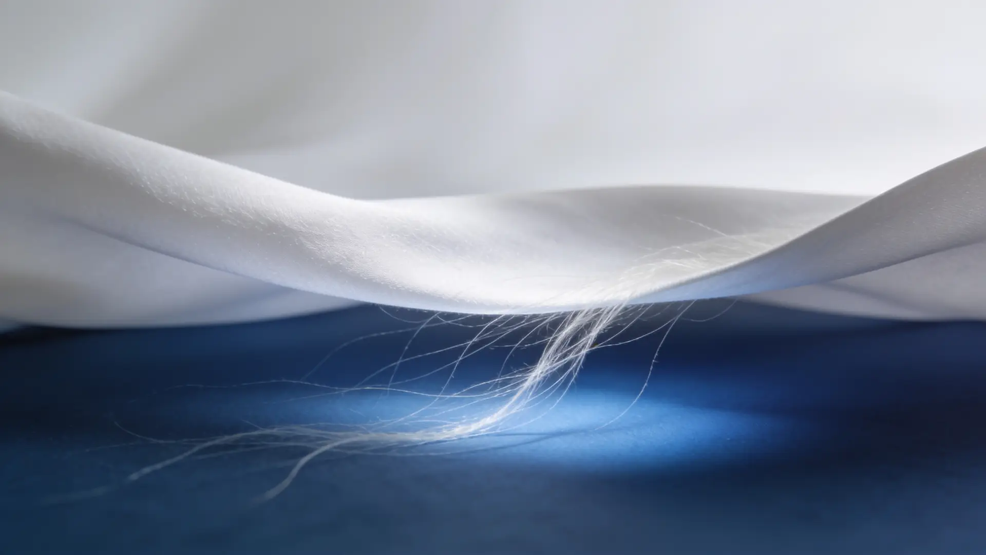 White fabric lifting as fine threads release beneath it — illustrative image for subcision